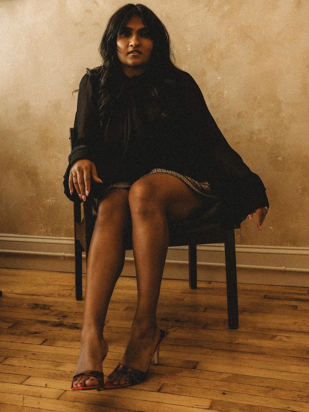 Mashi J seated in a chair on a wood floor